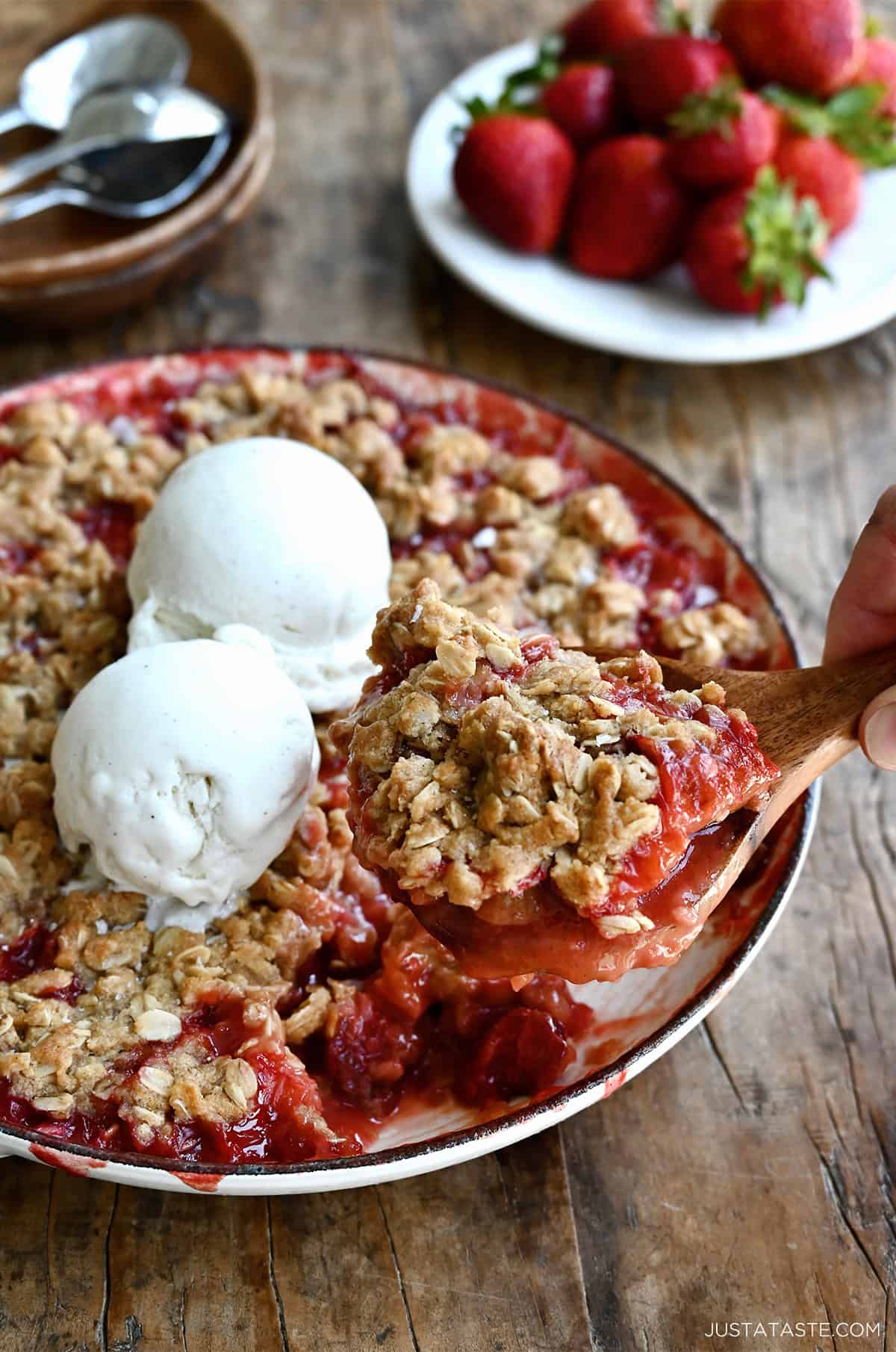 Strawberry rhubarb crisp in a baking dish, topped with two scoops of vanilla ice cream.