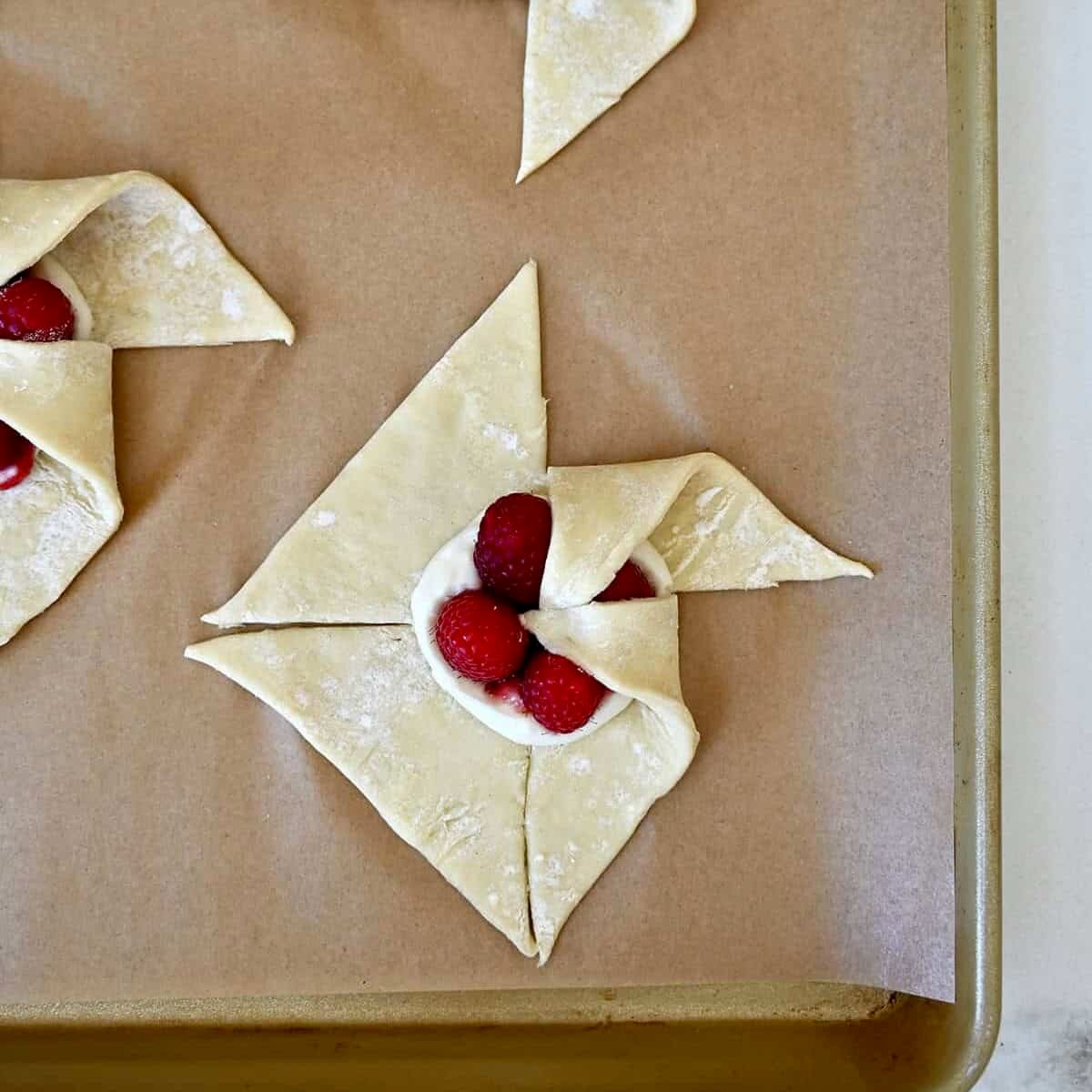Step 2 in shaping a pinwheel puff pastry: Folding another corner of a cut section into the center.