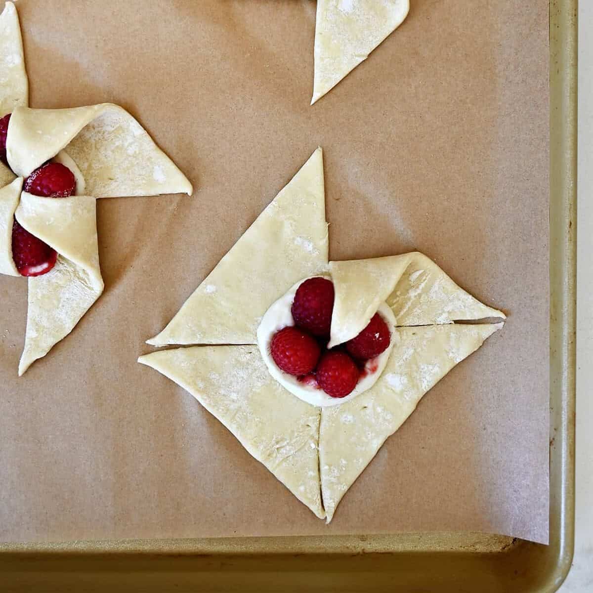Step 1 in shaping a pinwheel puff pastry: Folding one corner of a cut section into the center.