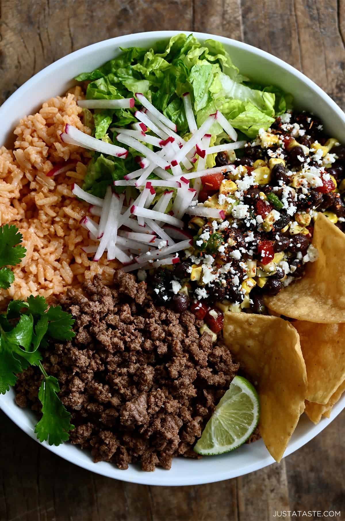 Ground beef taco bowl with shredded lettuce, Mexican rice, black bean and corn salsa, sliced radishes, and tortilla chips.