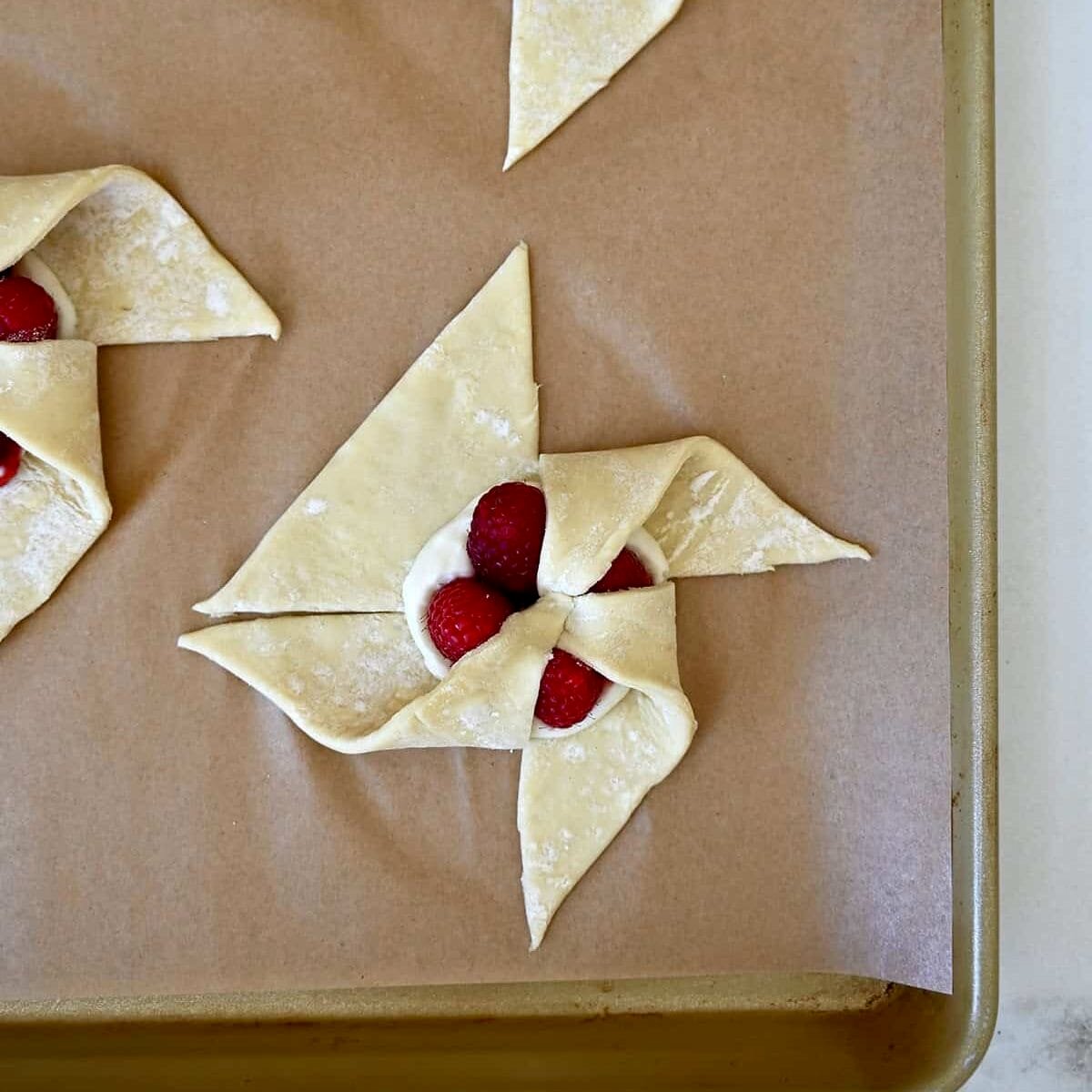 Step 3 in shaping a pinwheel puff pastry: Folding another corner of puff pastry into the center.