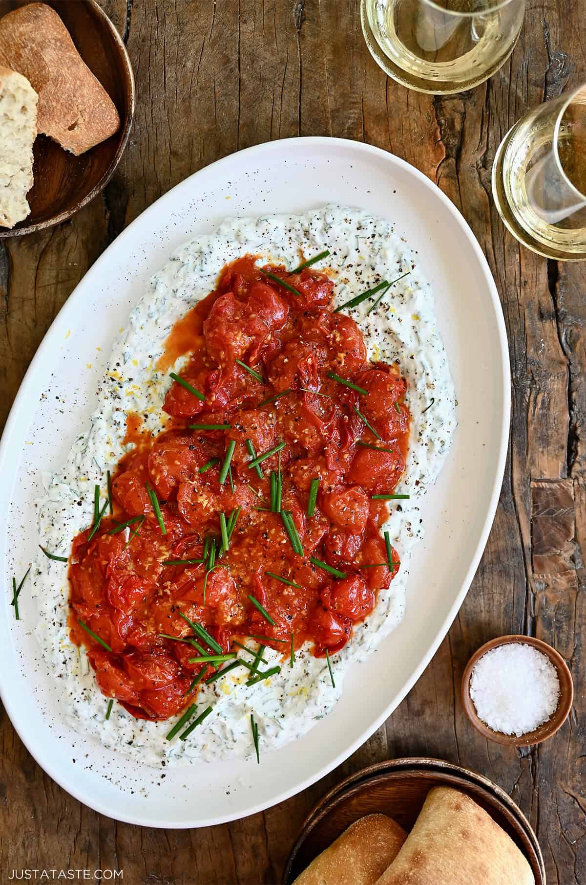 A white platter topped with whipped cottage cheese and jammy tomatoes with wine glasses