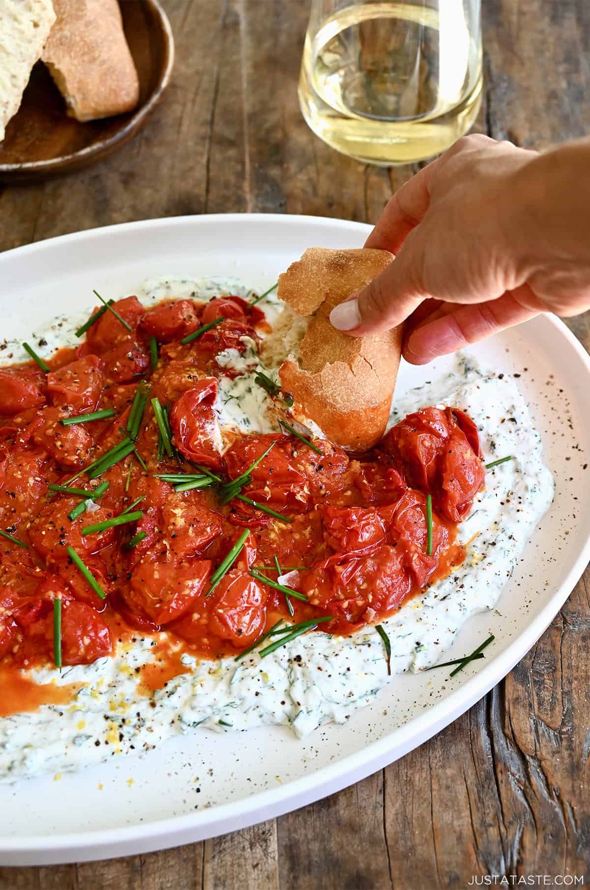 A hand dipping bread into a dip made with cottage cheese and tomatoes