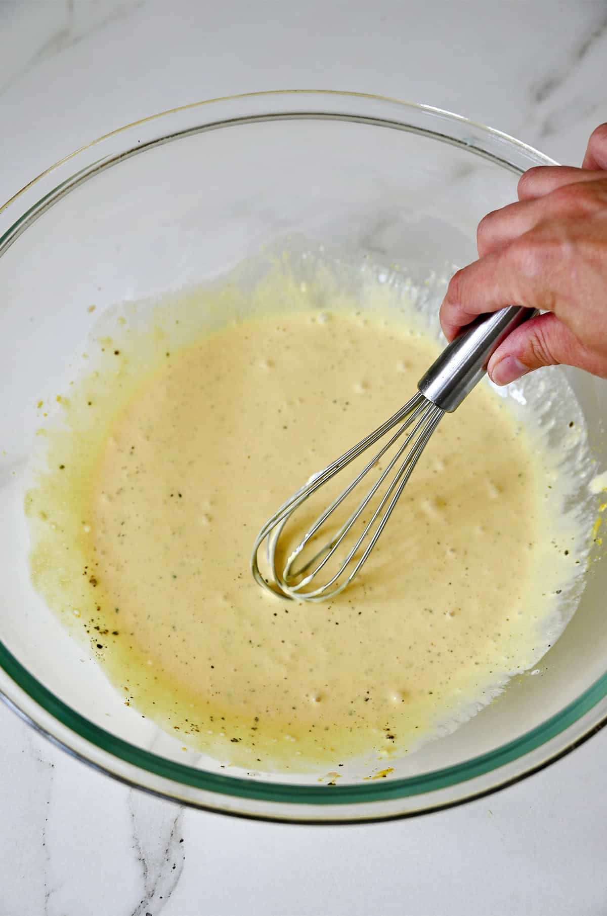 Creamy mayo-based pasta salad dressing is being whisked in a bowl.