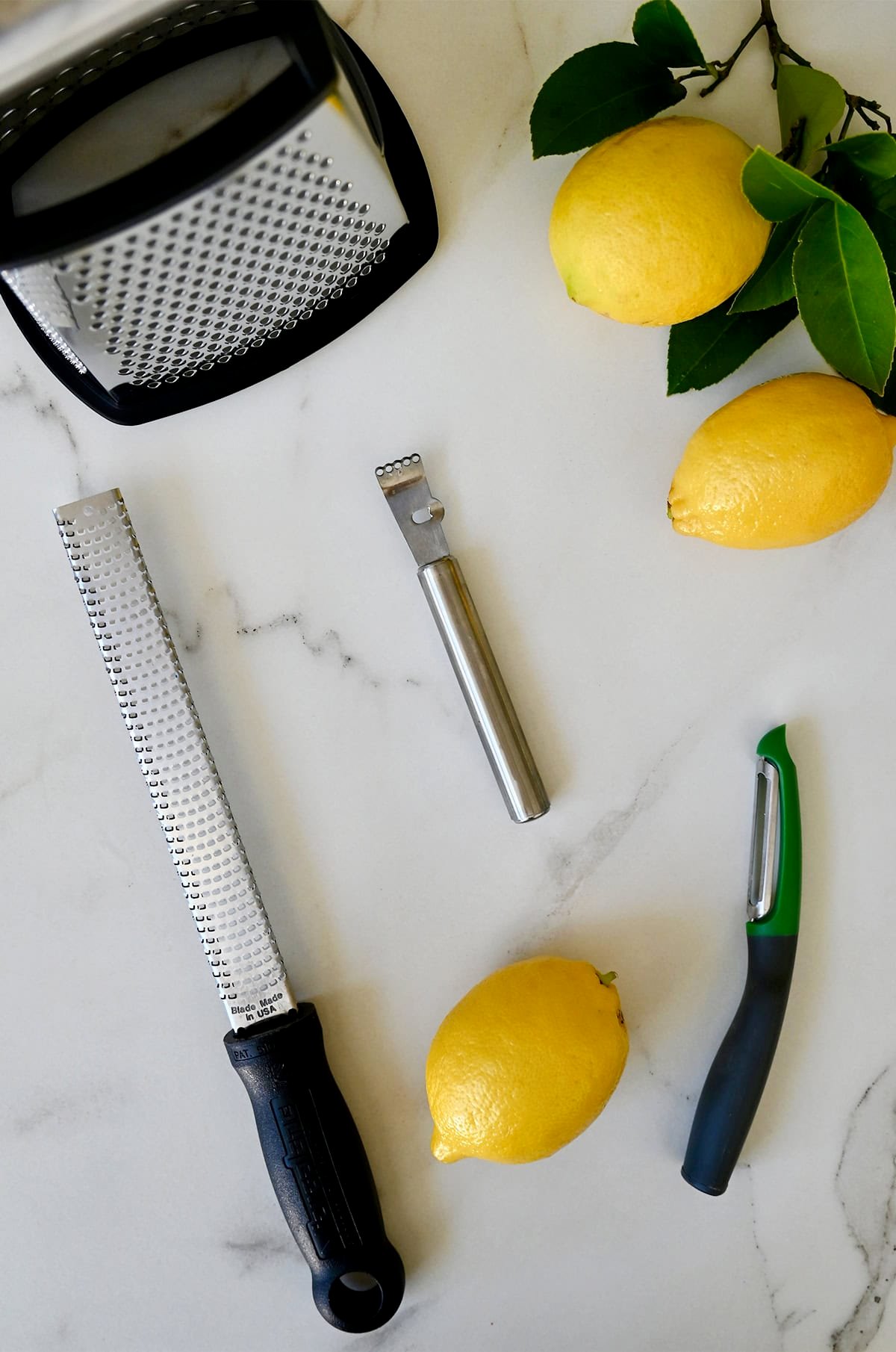 Lemons next to a box grater, a microplane, a vegetable peeler and a citrus peeler.