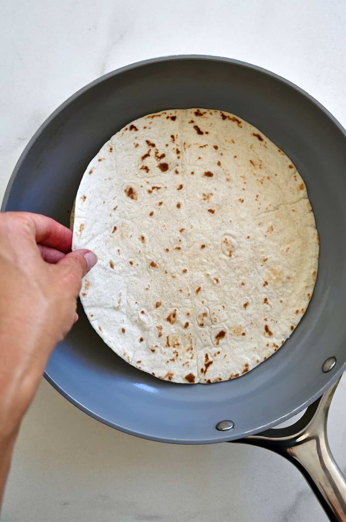 Adding a second tortilla atop a melty cheese tortilla in a skillet.
