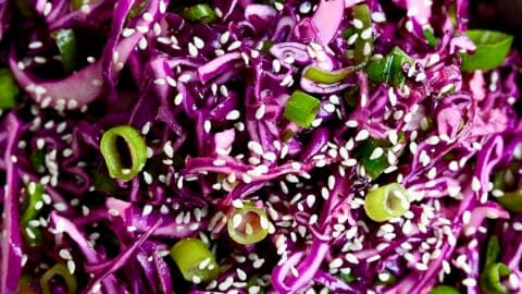 Asian slaw made with shredded purple cabbage, fresh lime juice, fish sauce and sesame oil in a large white serving bowl.