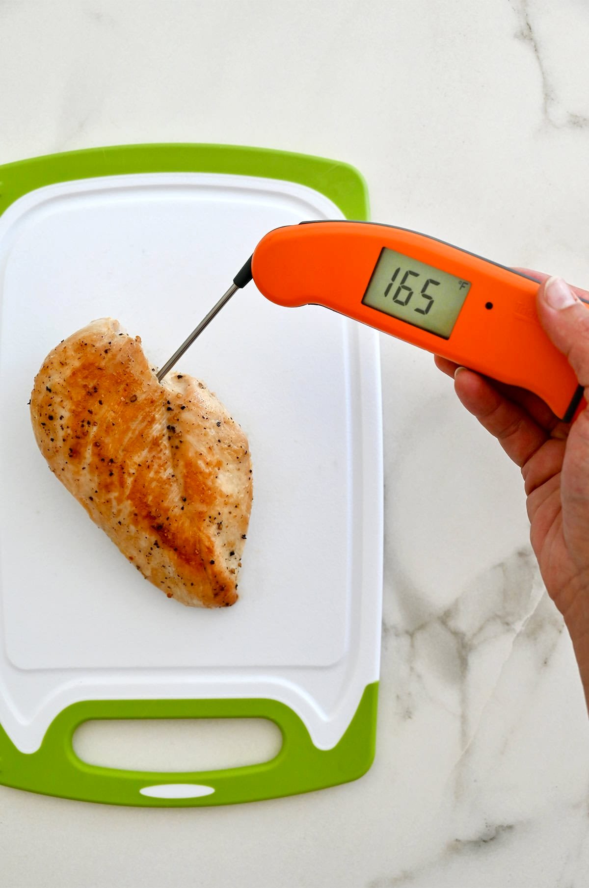 An instant-read meat thermometer inserted into the thickest part of a cooked chicken breast reads "165 degrees Fahrenheit."