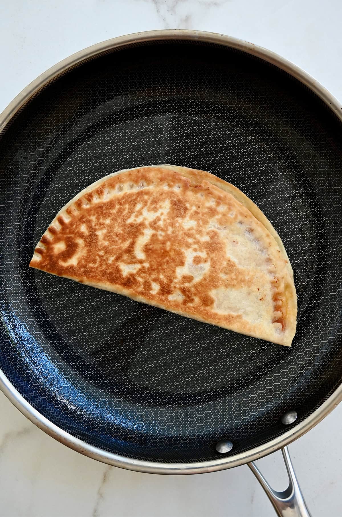 A golden brown and crisp moon-shaped quesadilla in a skillet. 