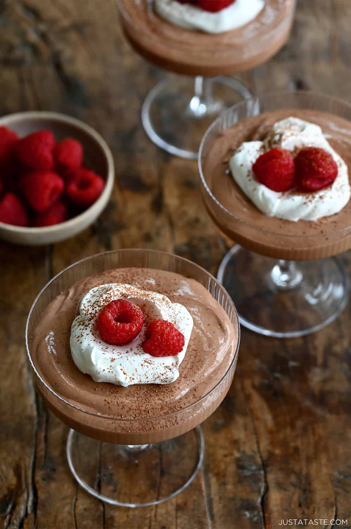 Three coupe glasses filled with chocolate mousse and sitting on a wooden surface