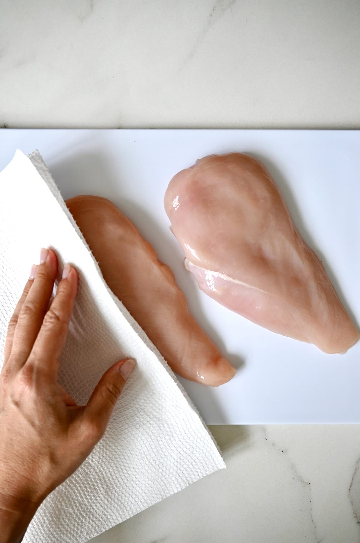 Using a power towel to pat a chicken breast dry before cooking in a pan.