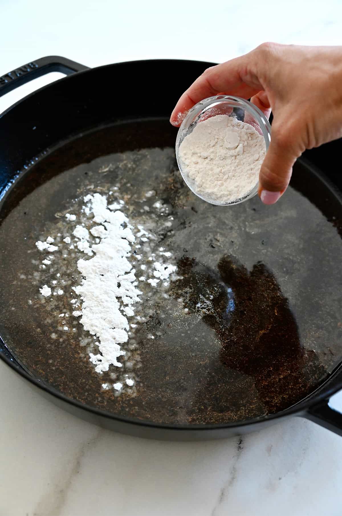Adding flour to a pan with drippings and melted butter.