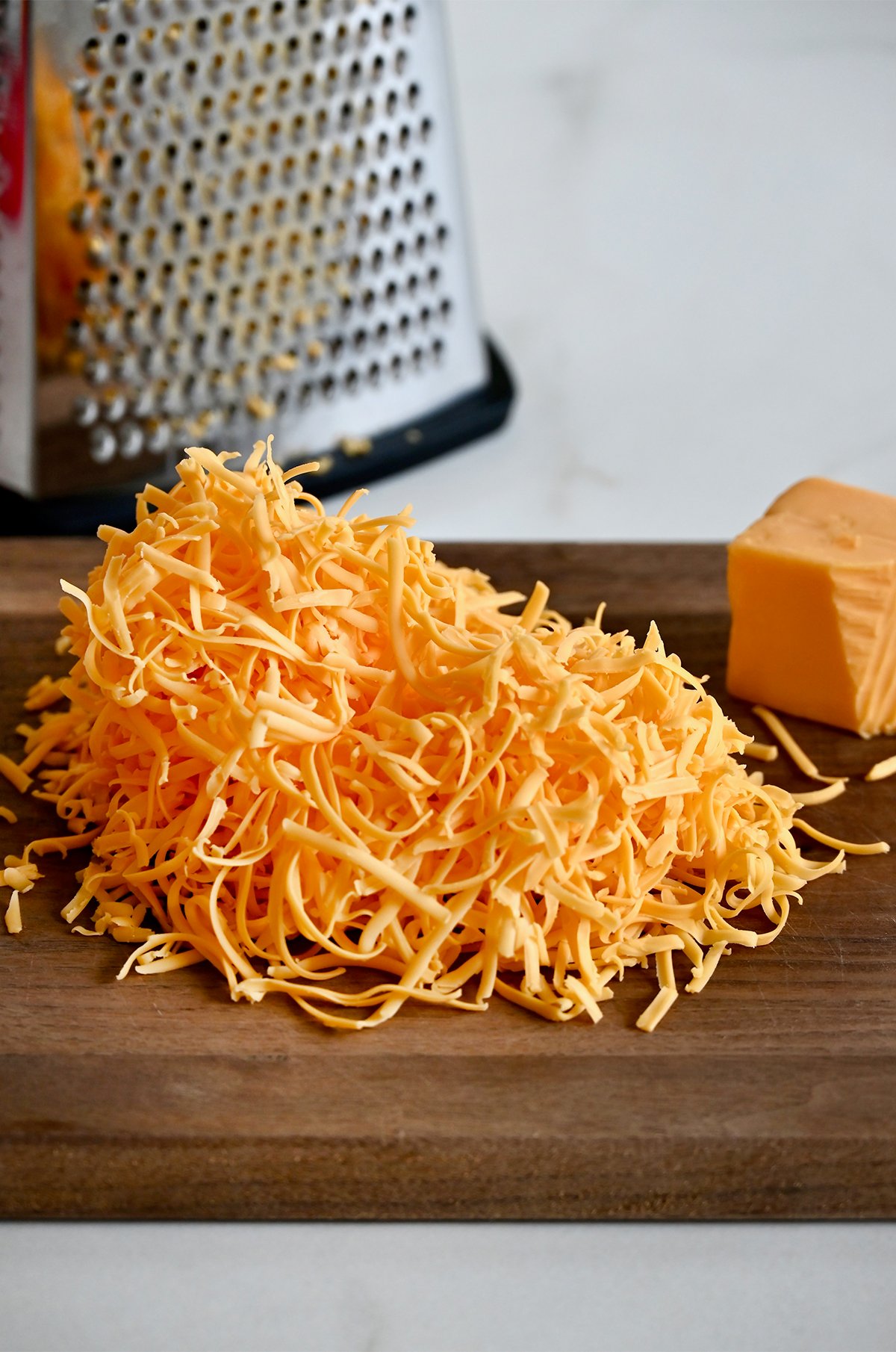 Freshly shredded cheddar cheese next to a box grater.