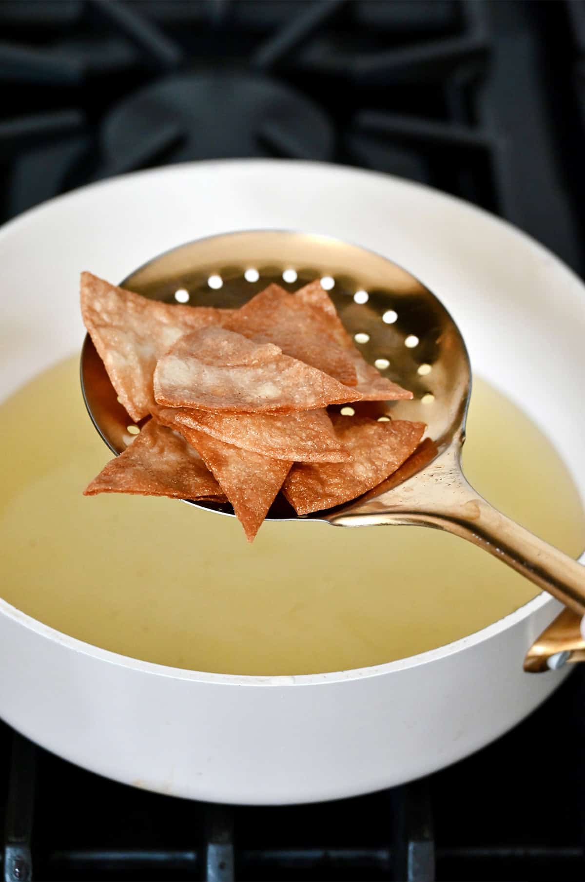 Fried tortilla chips on a slotted spoon above a large pot with hot oil.
