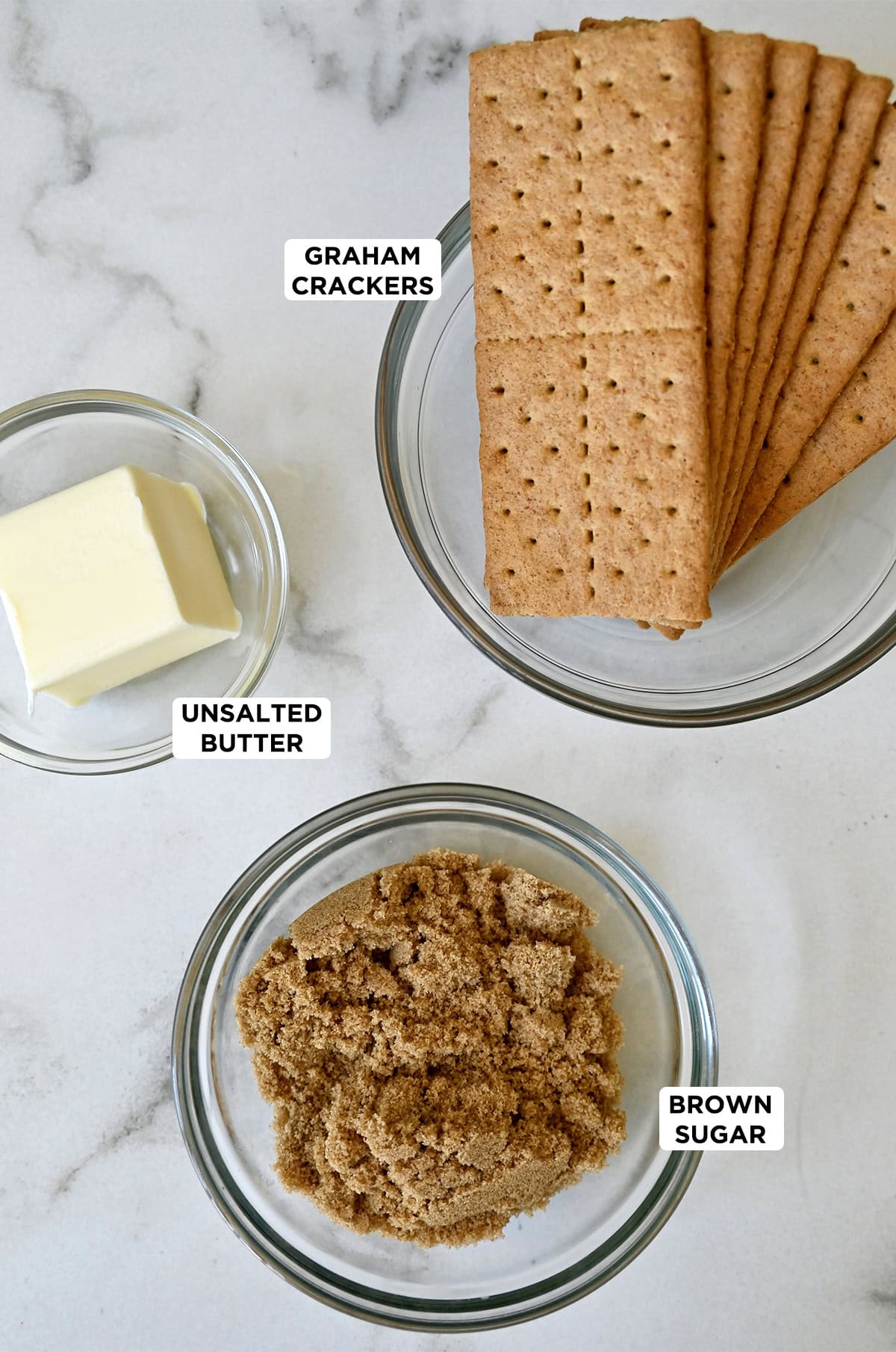 Three bowls containing graham crackers, unsalted butter and light brown sugar.