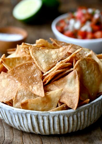 Homemade tortilla chips in a bowl near a small bowl filled with chunky salsa.