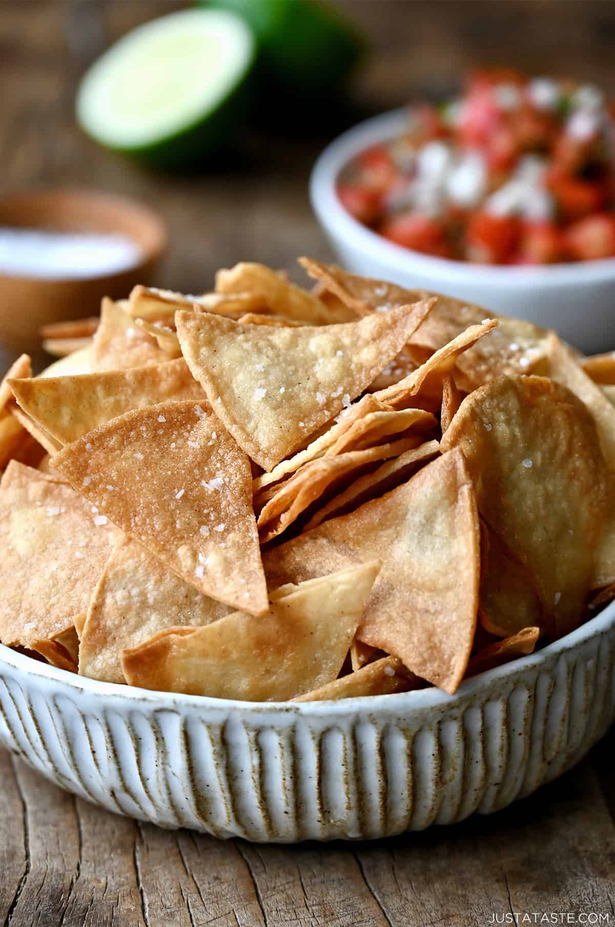 Homemade tortilla chips in a bowl near a small bowl filled with chunky salsa.