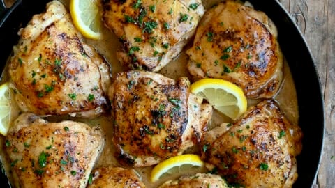 Easy lemon pepper chicken in a cast iron skillet with slices of lemon.
