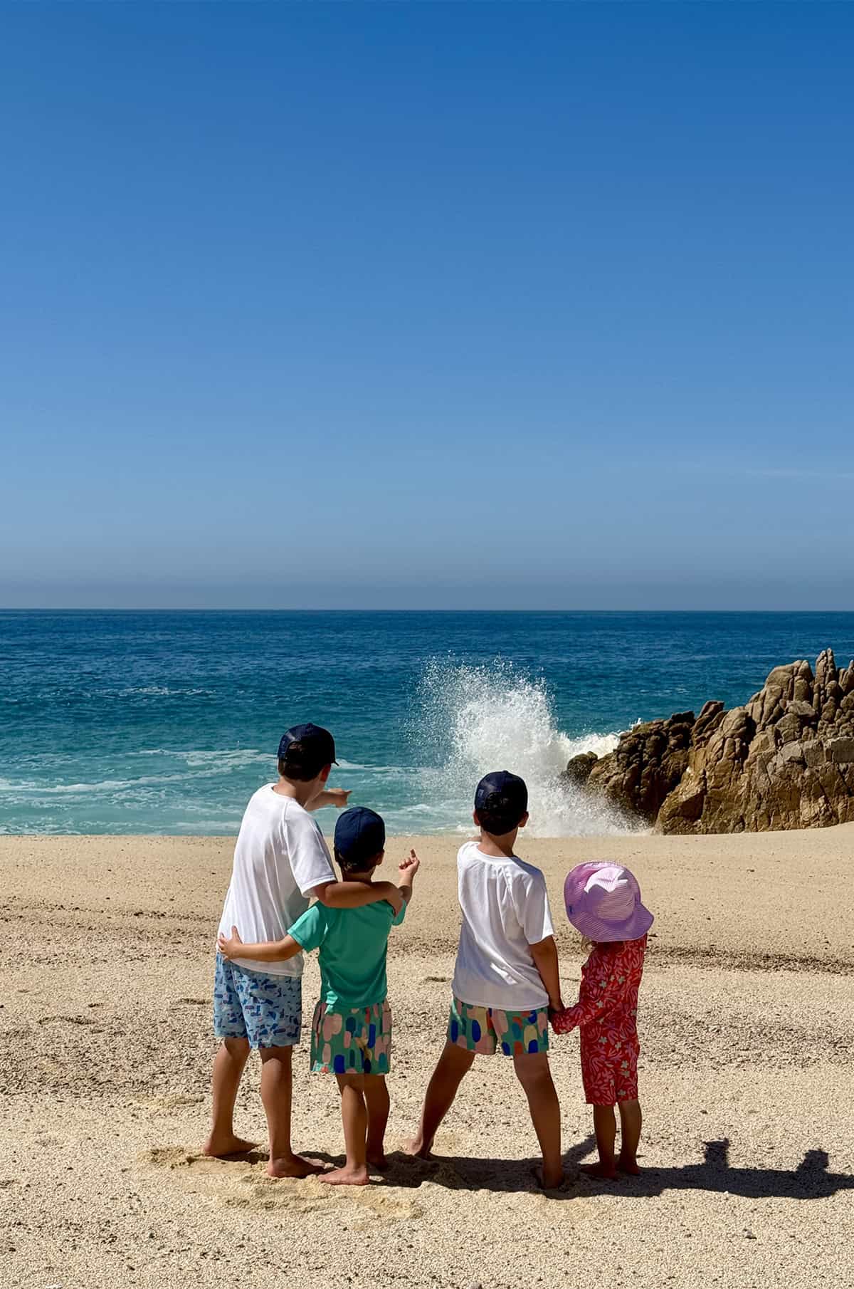 Four kids standing on a beach pointing at crashing waves