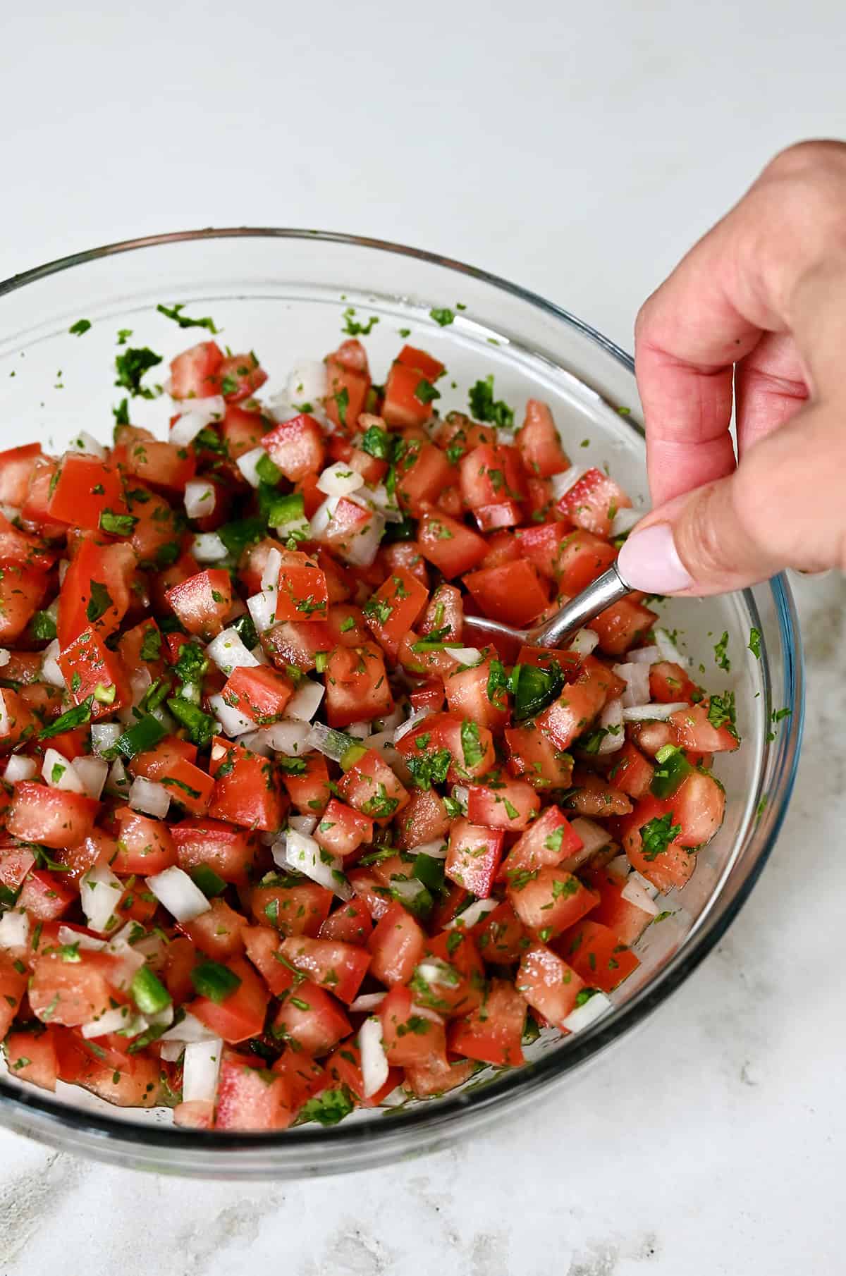 Mixing all the ingredients for pico de gallo in a bowl with a spoon.