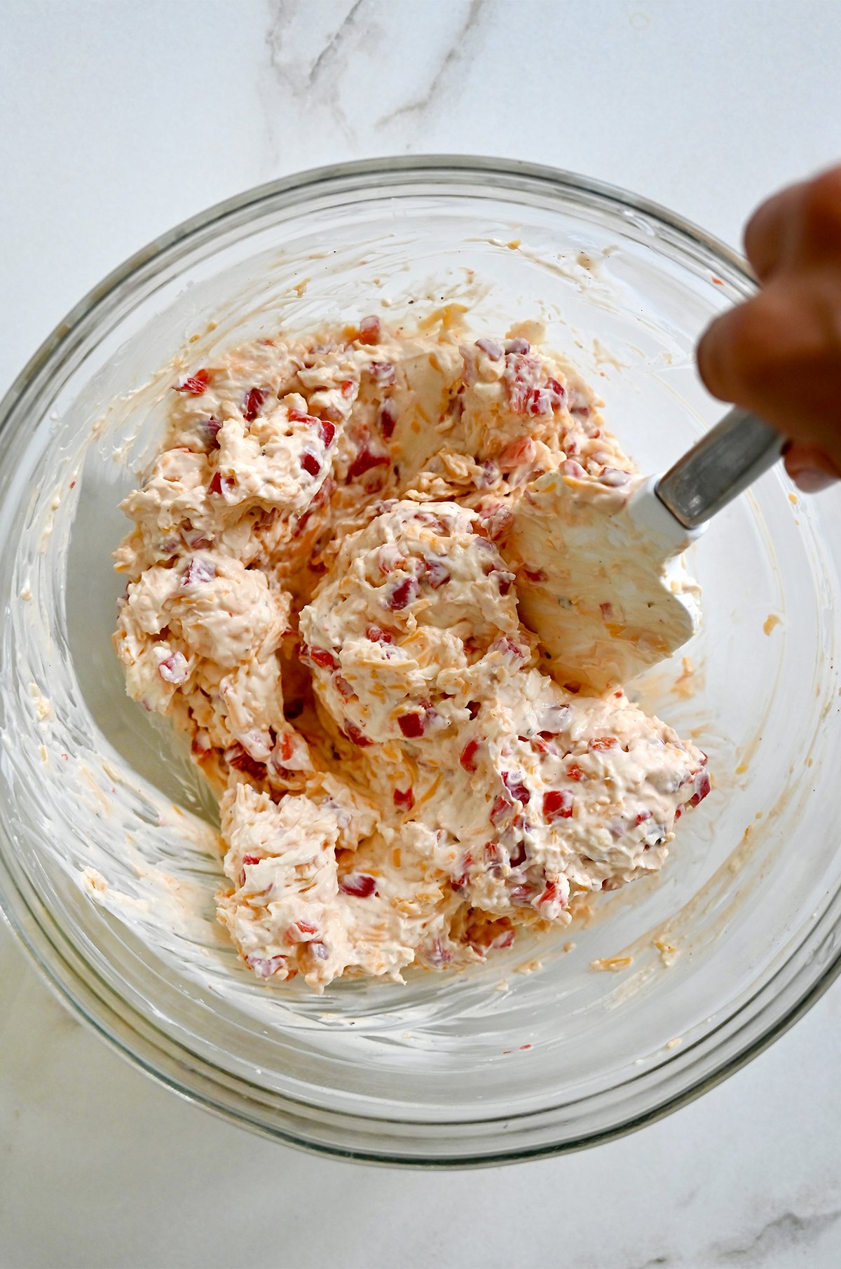Using a spatula to mix softened cream cheese, mayo, shredded cheddar cheese, and diced pimento peppers in a large bowl.