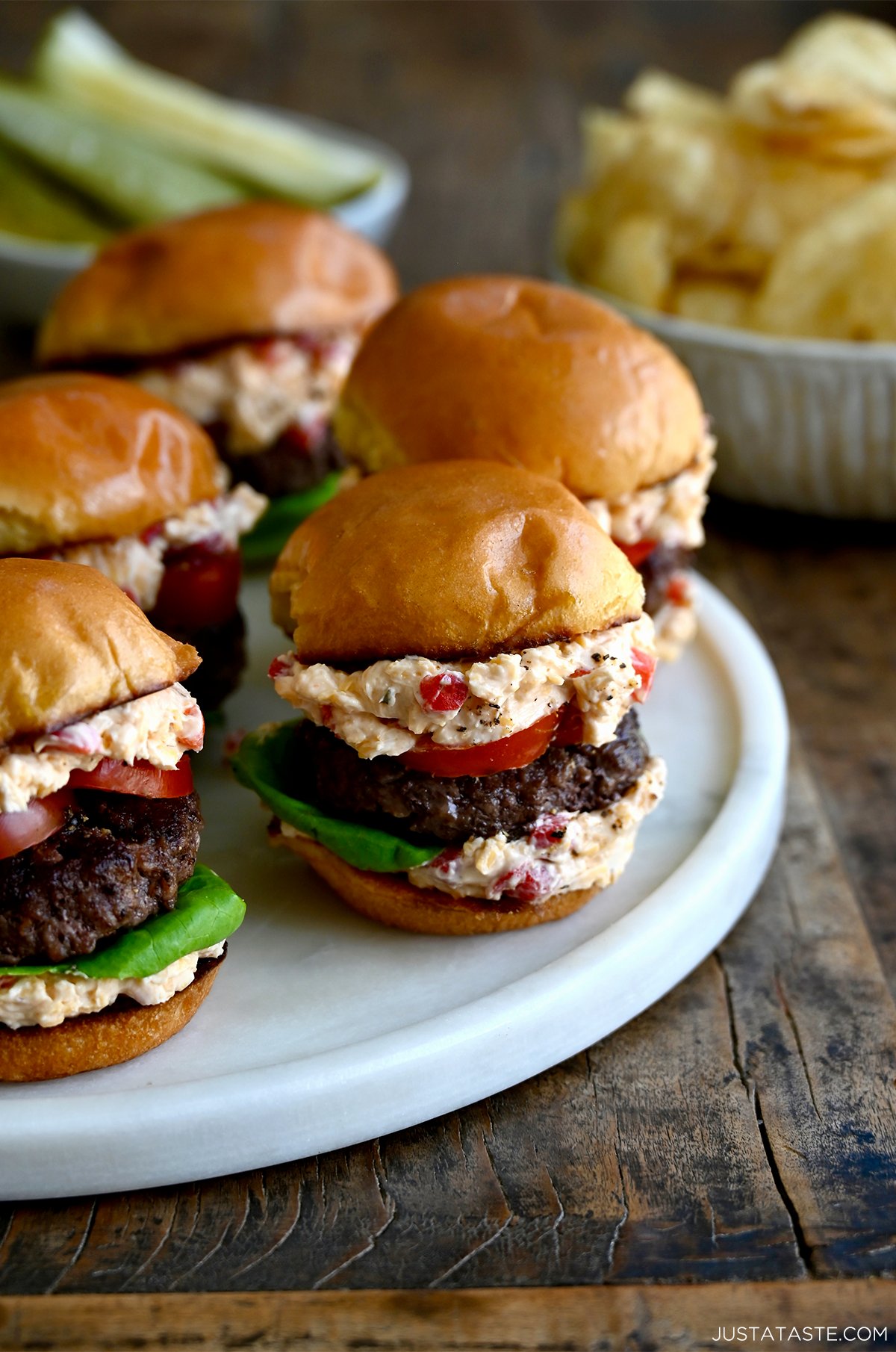 Several pimento cheeseburgers with a slice of tomato and lettuce on toasted buns.