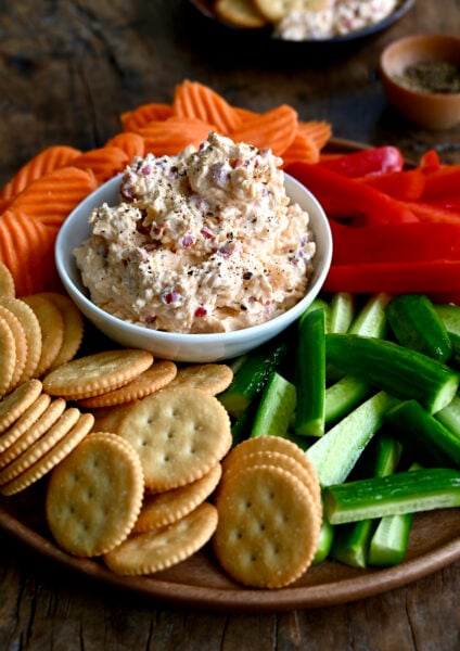 Pimento cheese dip in a small bowl, surrounded by crudités, on a serving platter.
