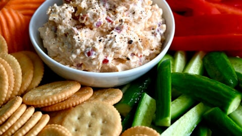 Pimento cheese dip in a small bowl, surrounded by crudités, on a serving platter.