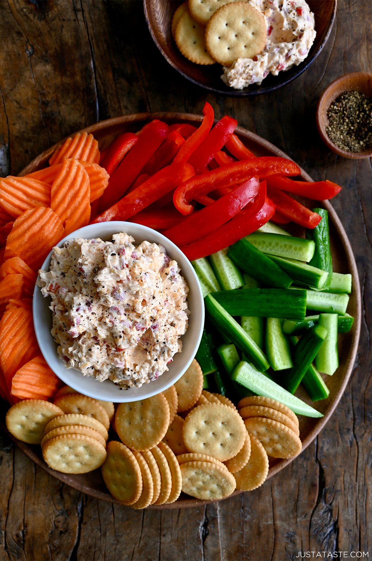 Homemade pimento cheese in a small bowl on a platter surrounded by Ritz crackers, sliced carrots, sliced bell pepper and sliced cucumber.