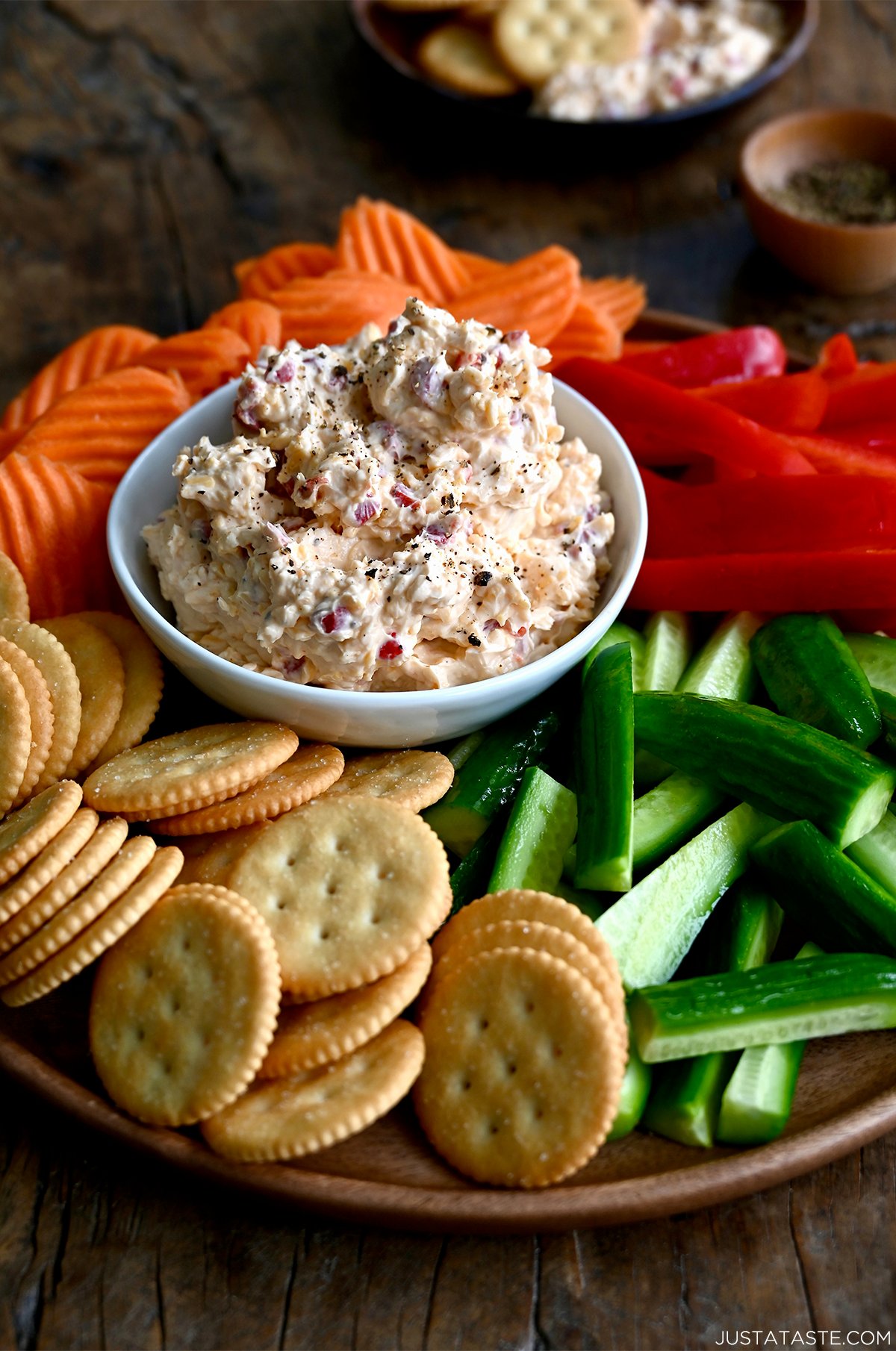 Pimento cheese dip in a small bowl, surrounded by crudités, on a serving platter.