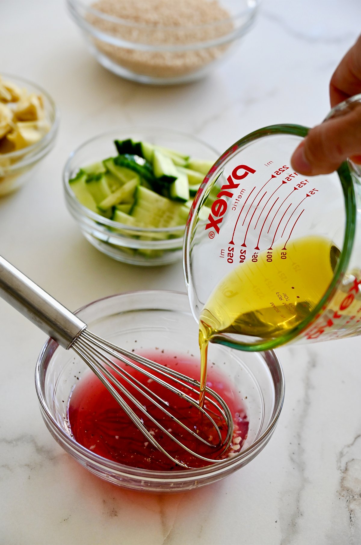 Pouring olive oil from a liquid measuring cup into a bowl with red wine vinegar and lemon juice to make a red wine vinaigrette.