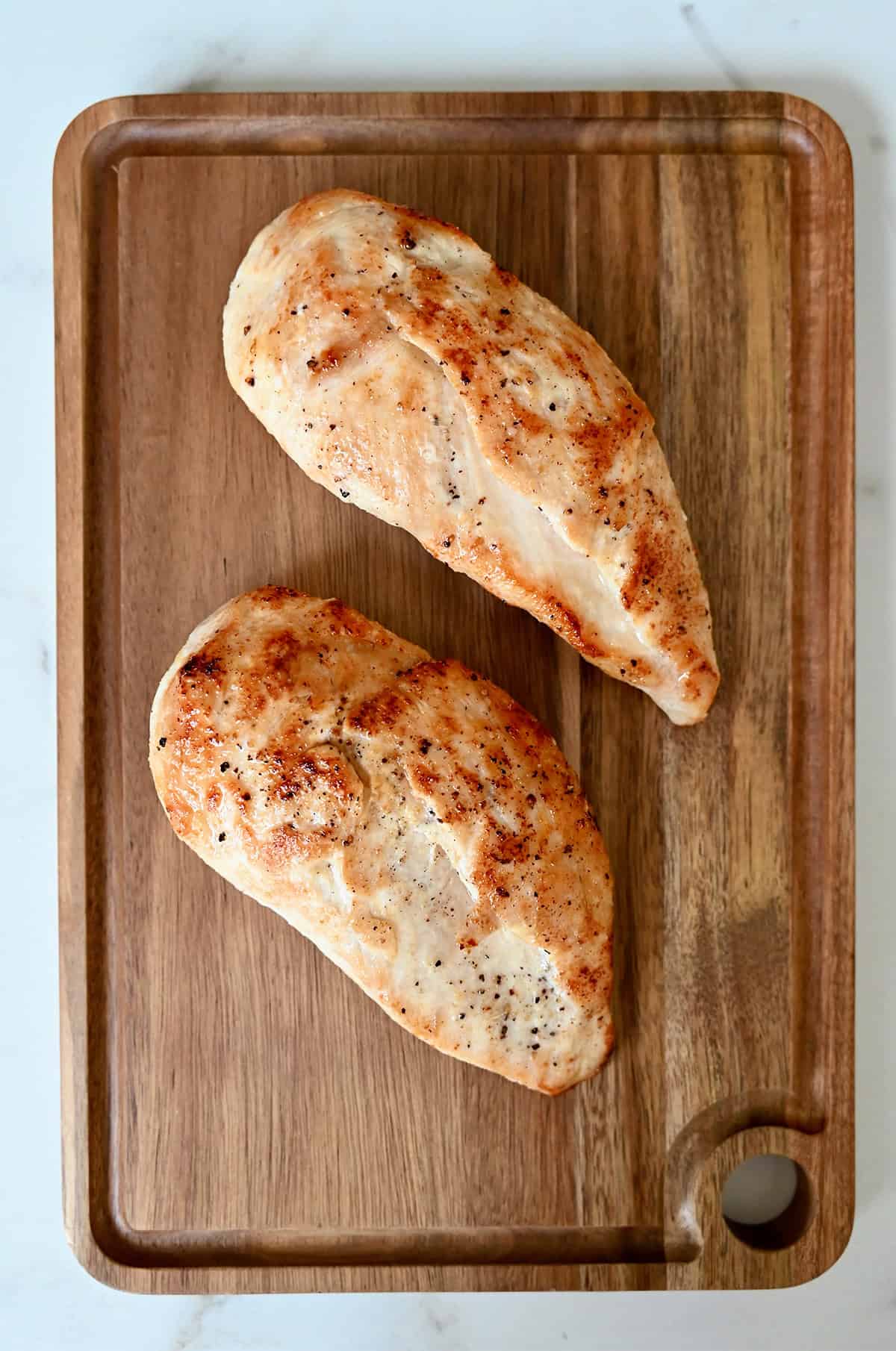 Two pan-fried chicken breasts resting on a cutting board to lock in juices.