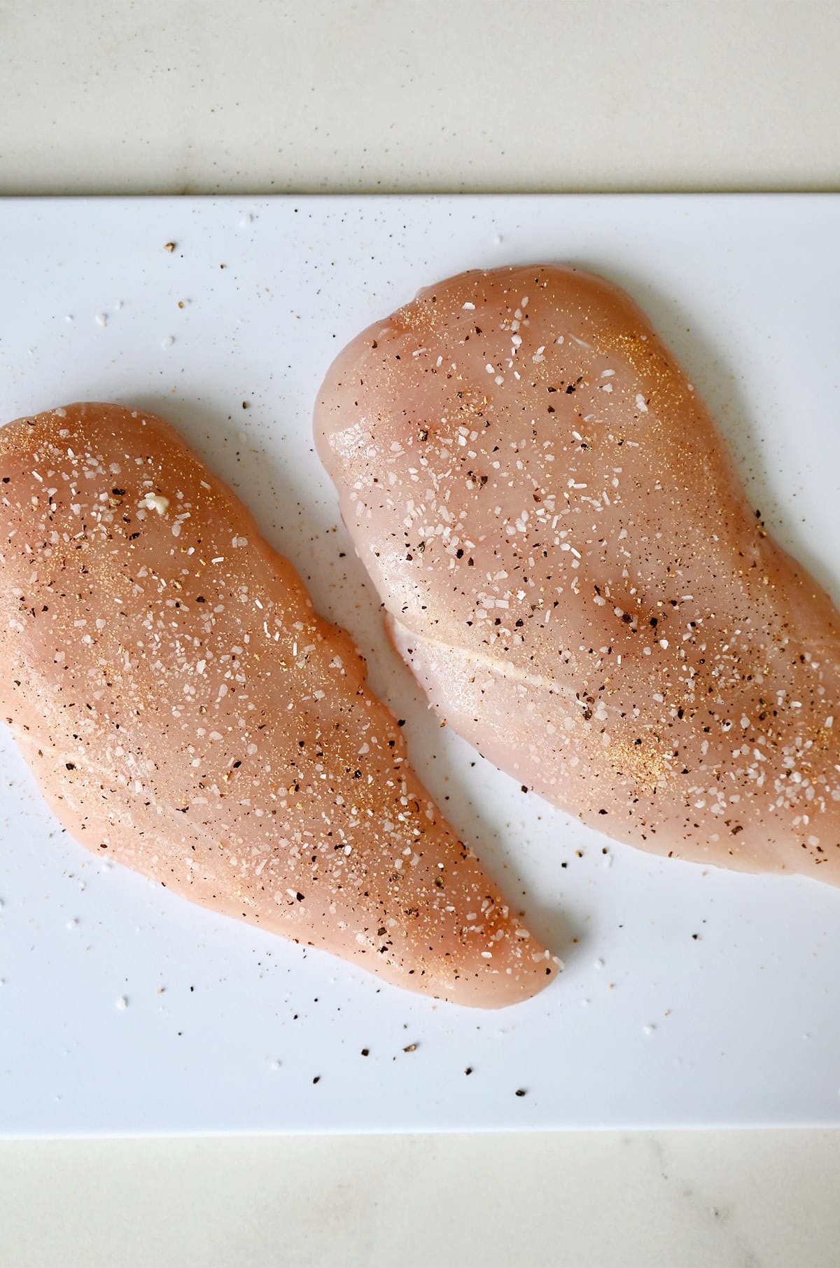Salt and pepper-seasoned chicken breast on a cutting board.