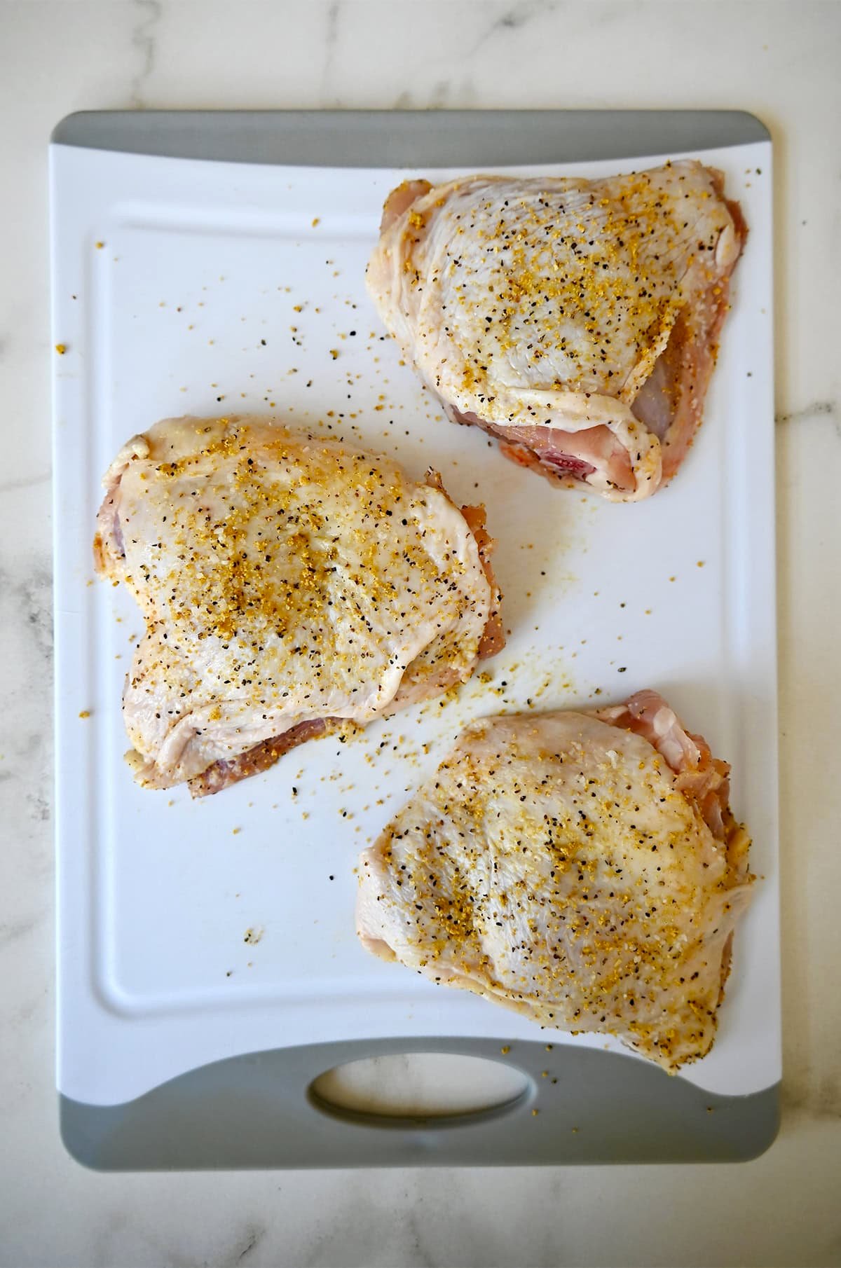 Boneless, skin-on chicken thighs seasoned with lemon pepper seasoning.