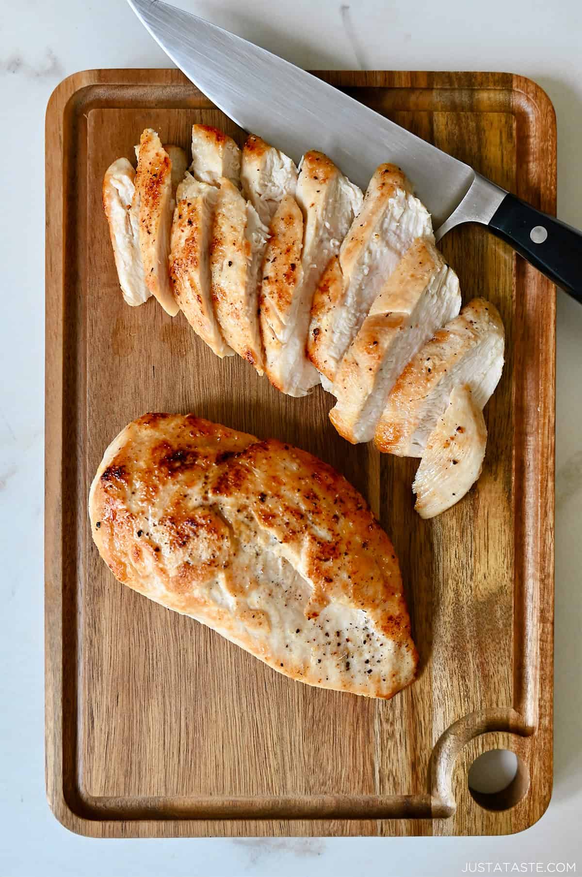 Sliced chicken breasts on a cutting board next to a sharp knife.