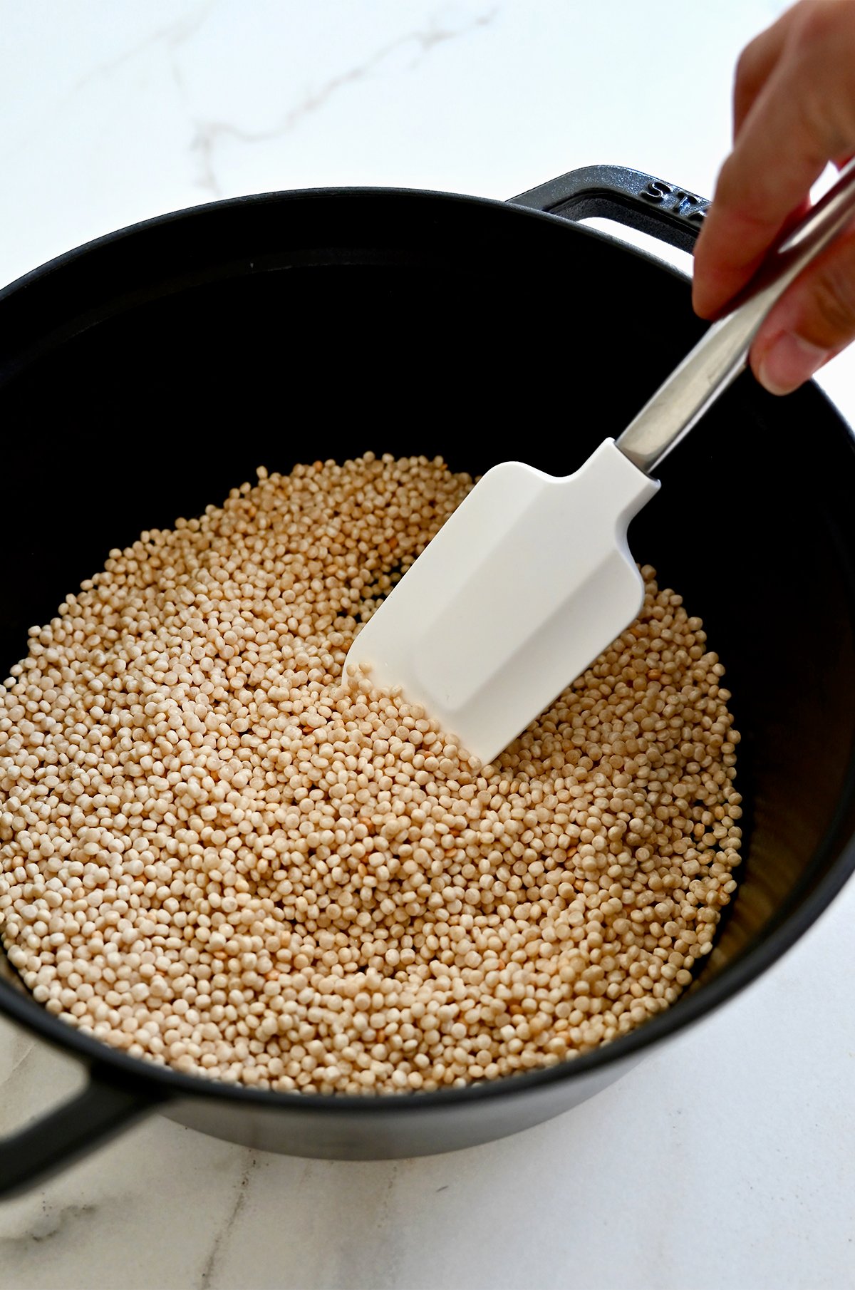 Toasted couscous in a pan with a white spatula.