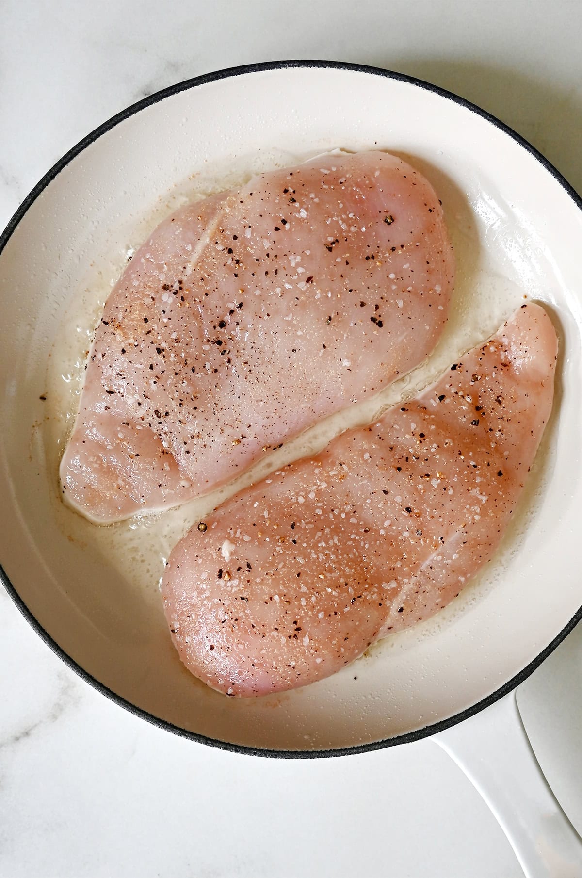 Searing the first side of two chicken breasts in a pan on a stovetop.