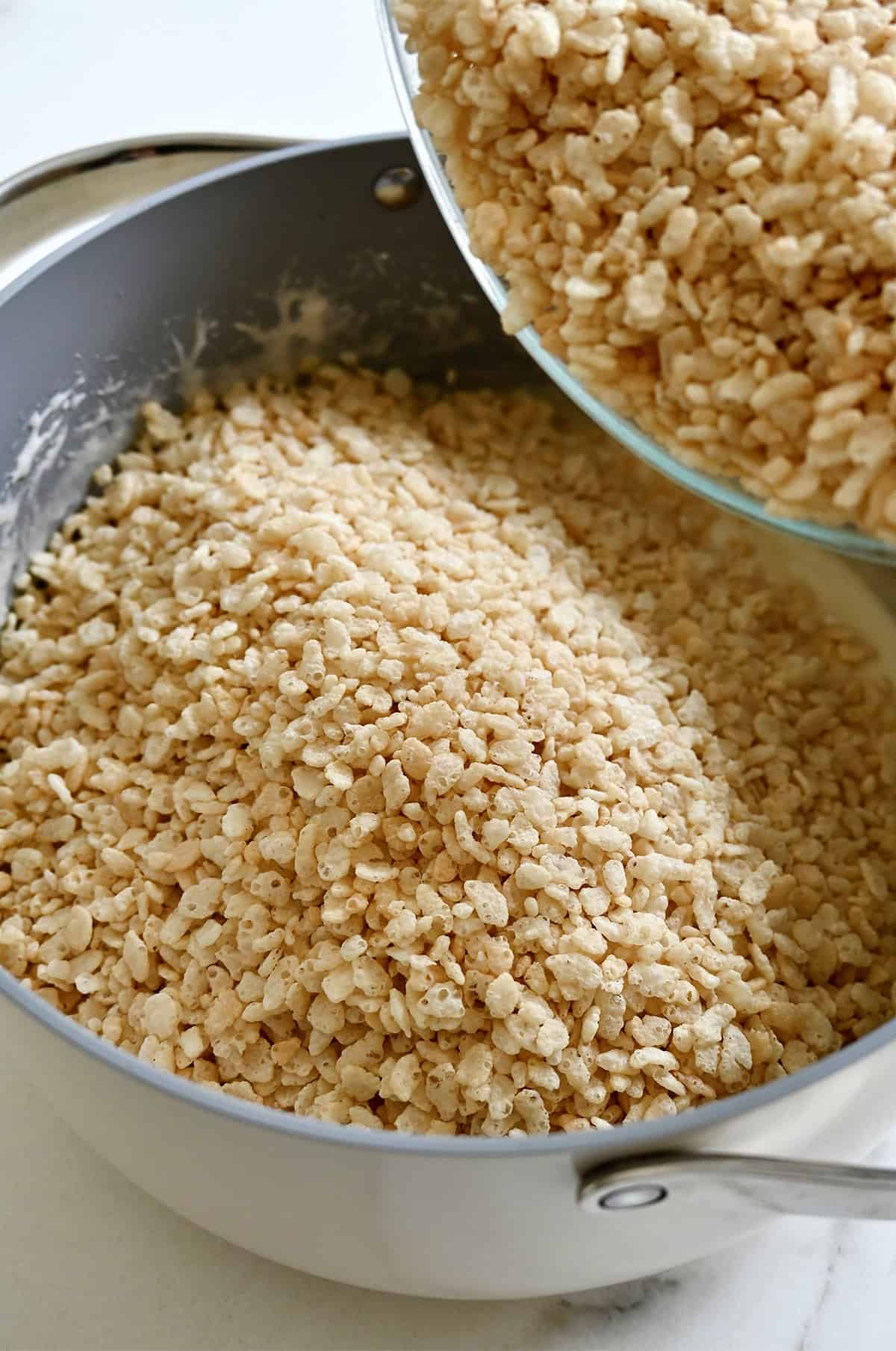Adding Rice Krispies cereal to a stockpot containing a mixture of melted marshmallows and butter.
