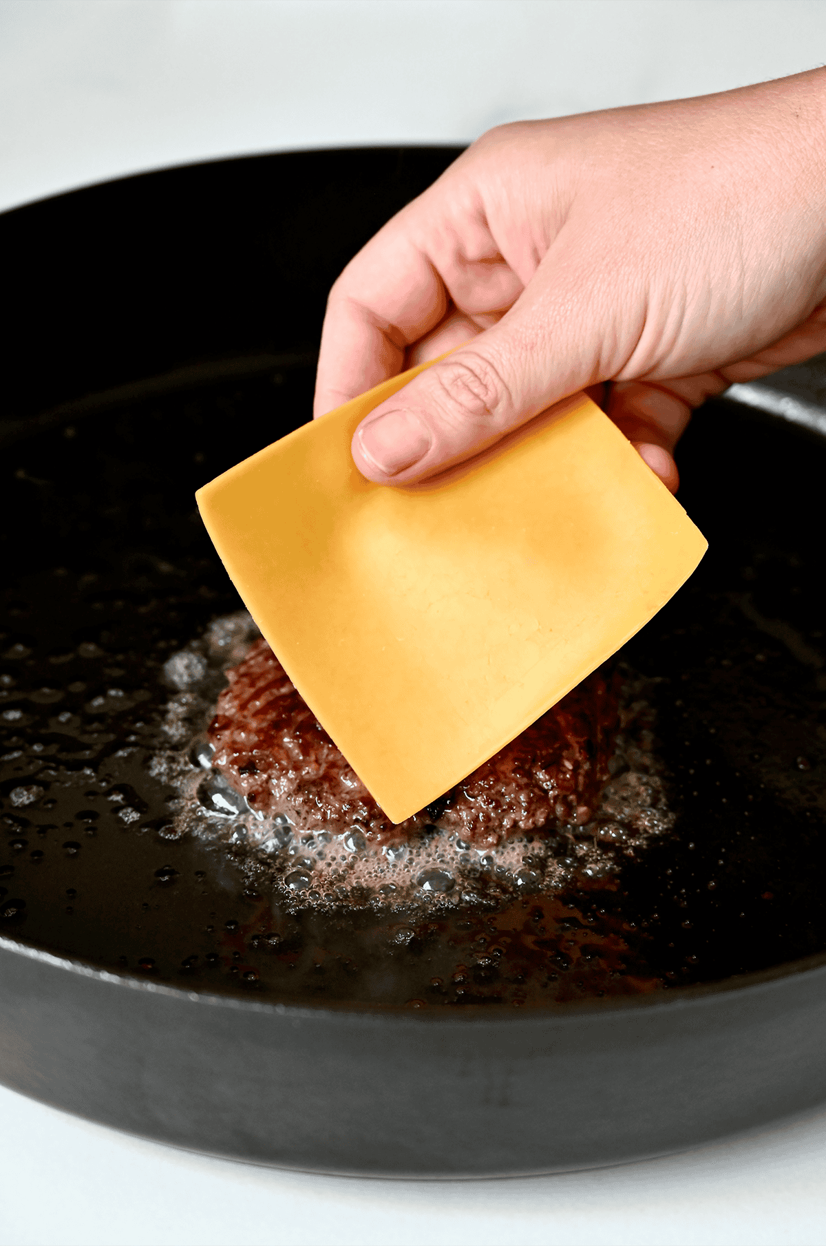 Adding a slice of cheddar cheese to a cooked hamburger patty.