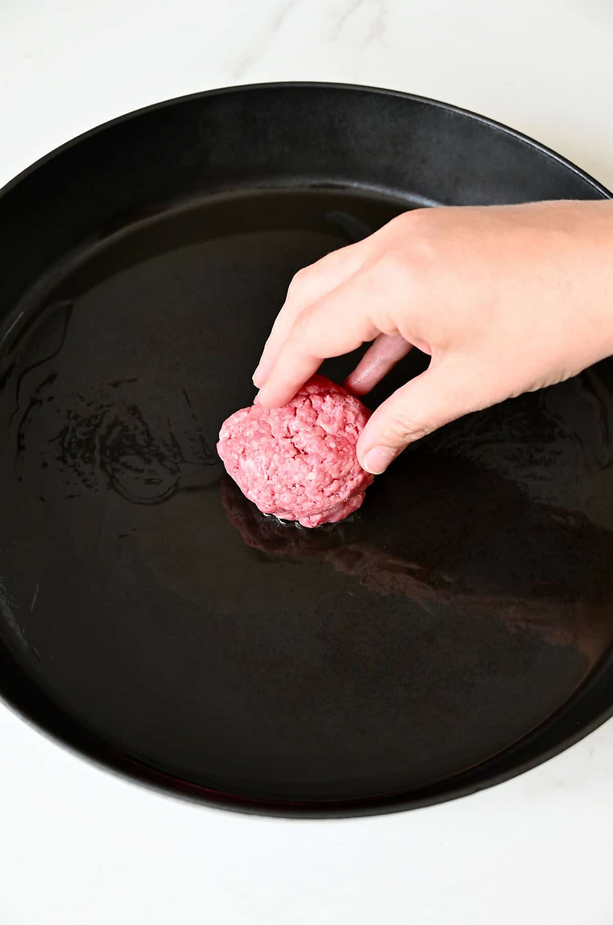 Adding a beef patty to a hot skillet with oil.