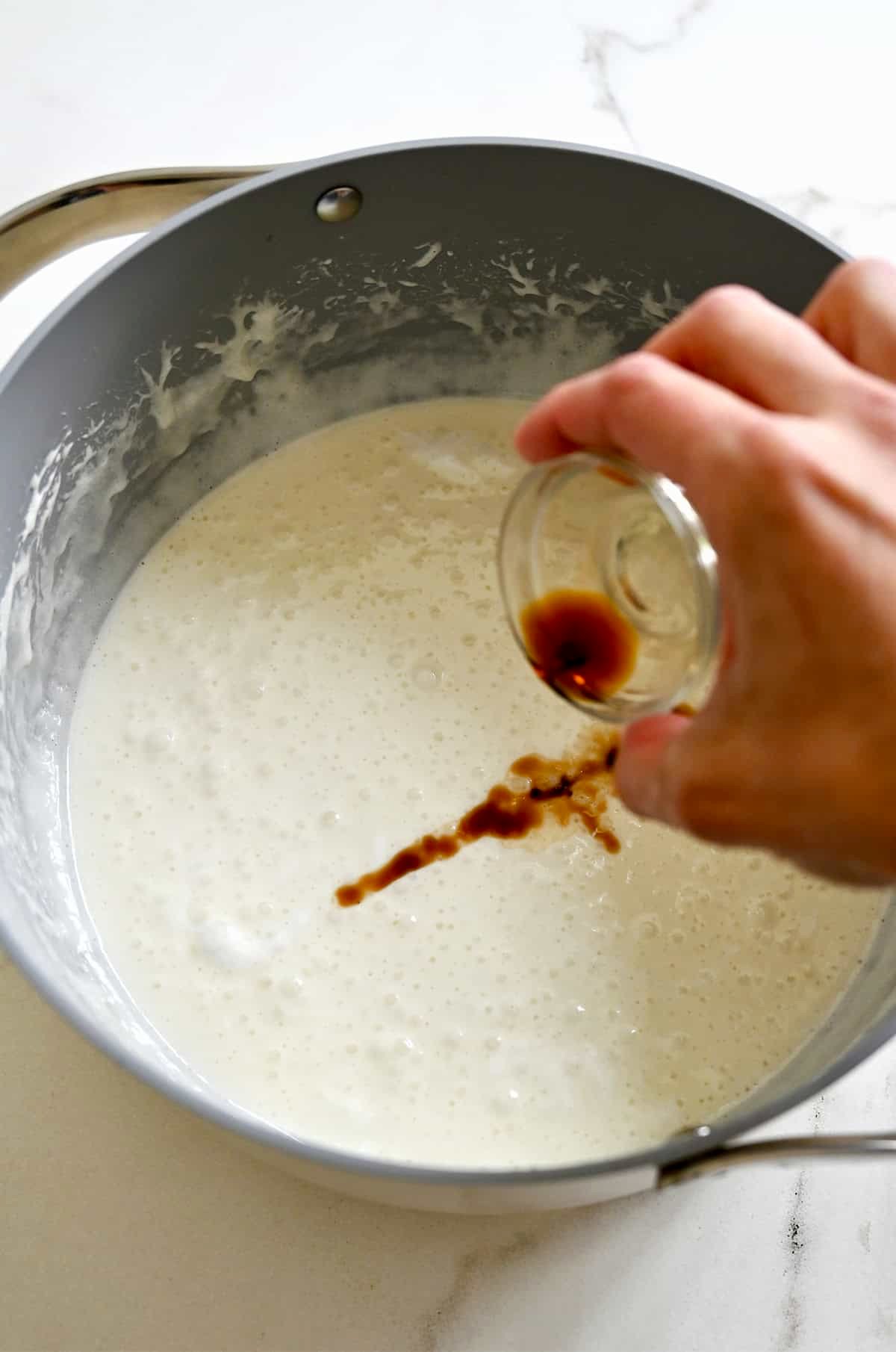 Adding vanilla to a large stockpot containing a melted butter and marshmallow mixture.
