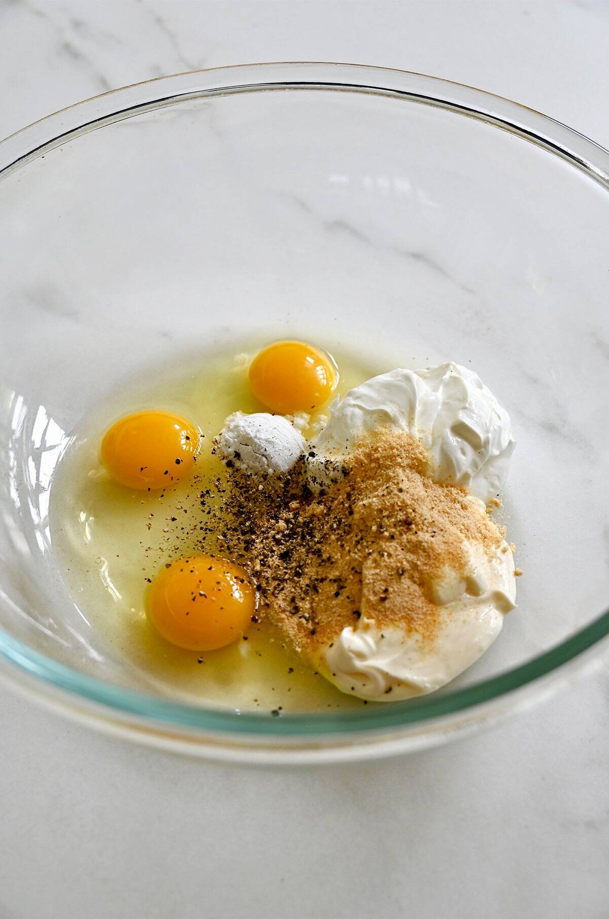 Sour cream, mayonnaise, garlic powder, onion powder, baking powder and eggs with ¼ teaspoon black pepper in a glass bowl.