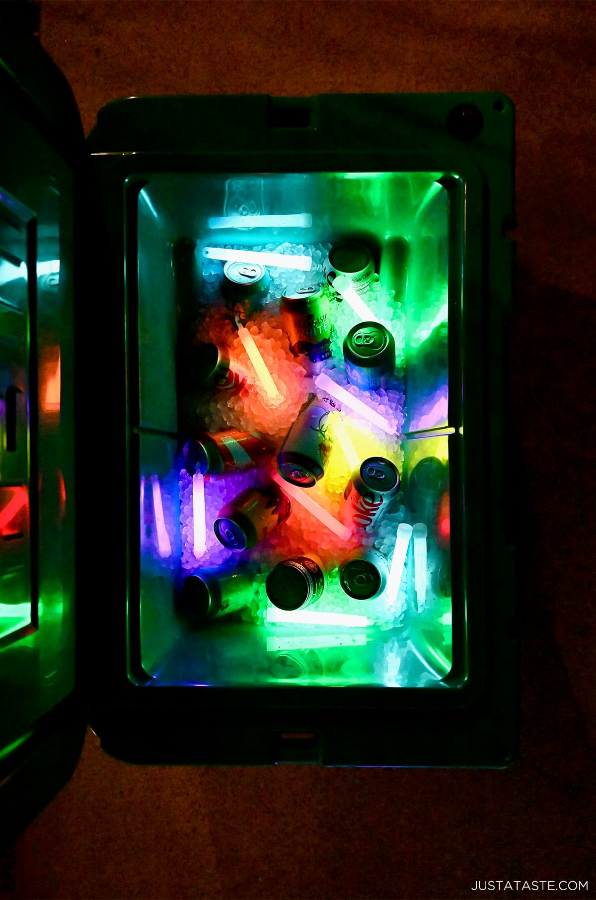 A cooler with ice, soda cans and glow sticks.