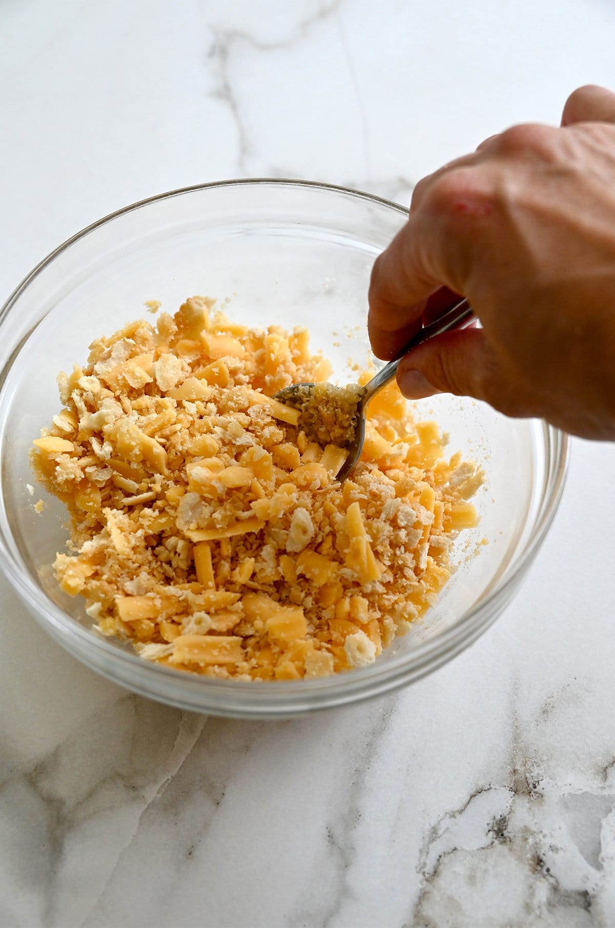 Crushed Ritz crackers being stirred together with melted butter and shredded cheddar to make a cheesy cracker topping for zucchini casserole.
