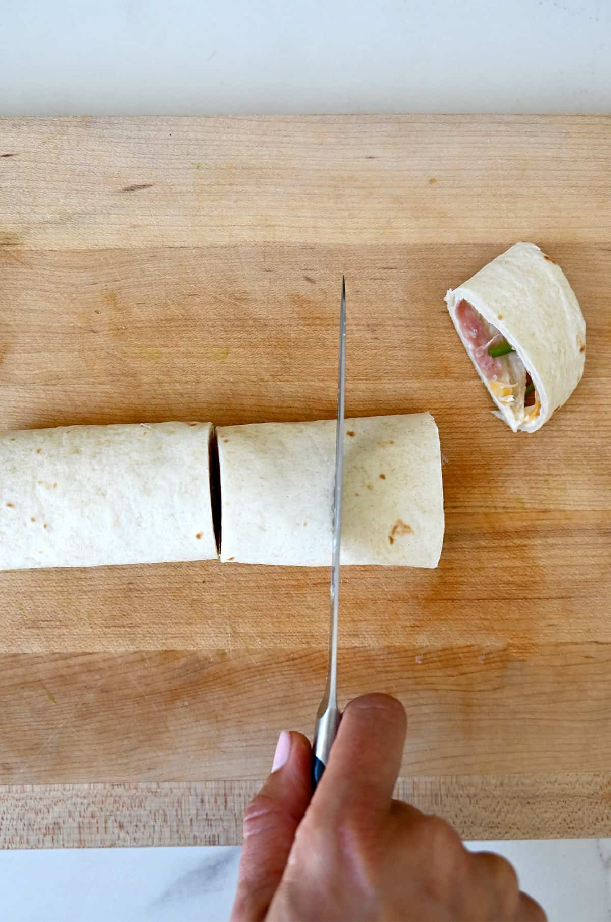Cutting a tortilla roll-up into pinwheel sandwiches.