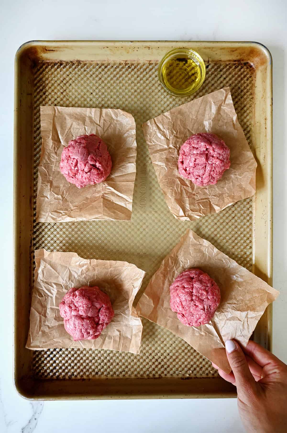 Four balls of ground beef on squares of parchment paper.