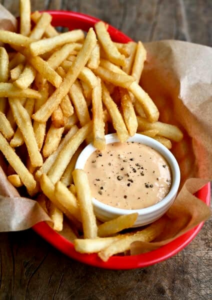 Homemade burger sauce in a small bowl in a red food basket with French fries.