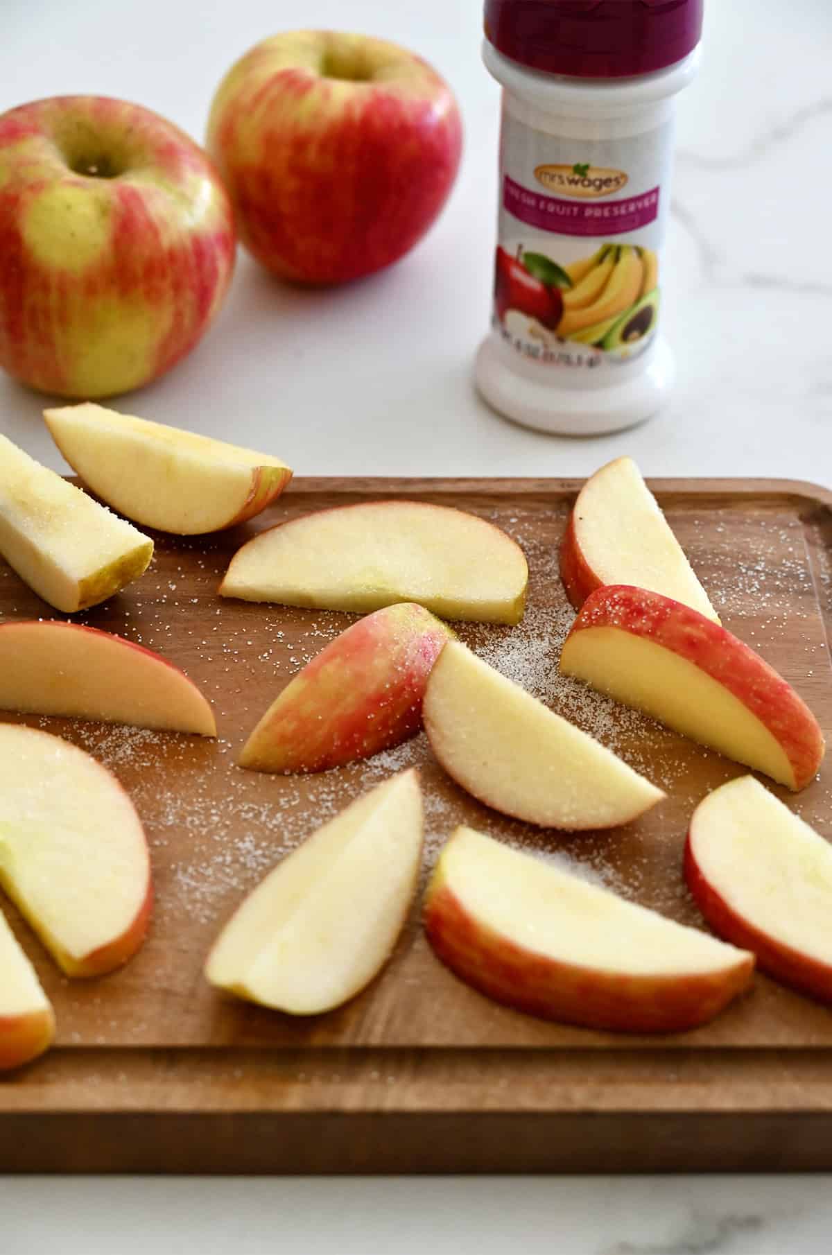Apple slices sprinkled with a fruit preserver on a cutting board.