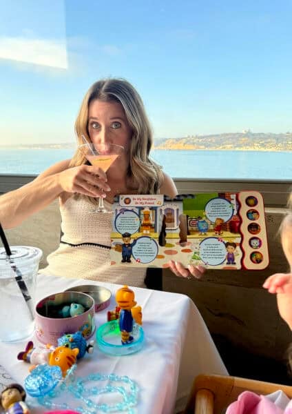 Girl at fancy restaurant reading a Daniel Tiger book while sipping a Cosmopolitan cocktail