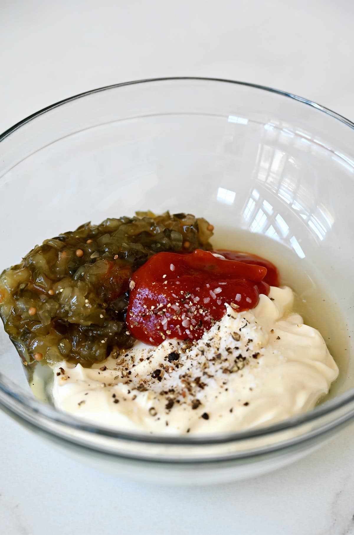 Pickle relish, ketchup, mayonnaise and apple cider vinegar in a bowl before being mixed together.